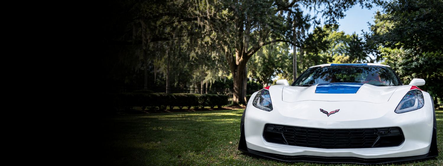 White sports car with blue stripe on a grassy area with trees in the background