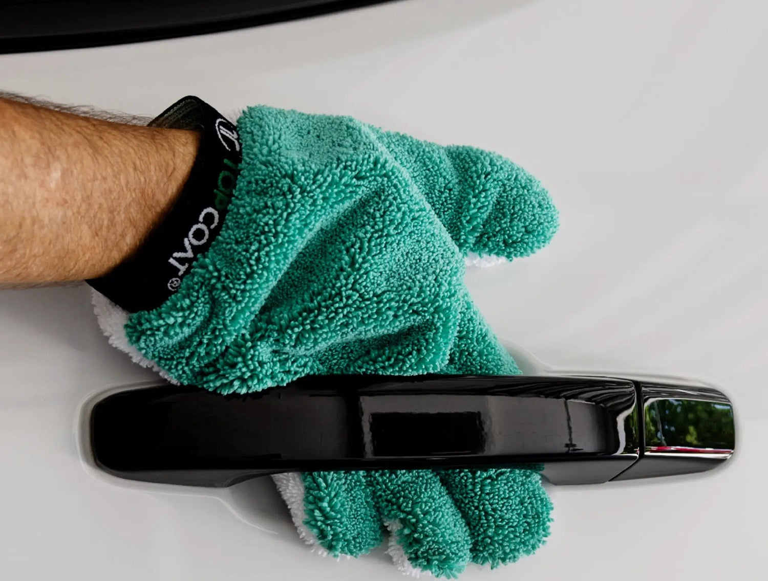Person cleaning a car door handle with a green microfiber cloth, featuring TopCoat LuvGluv branding.