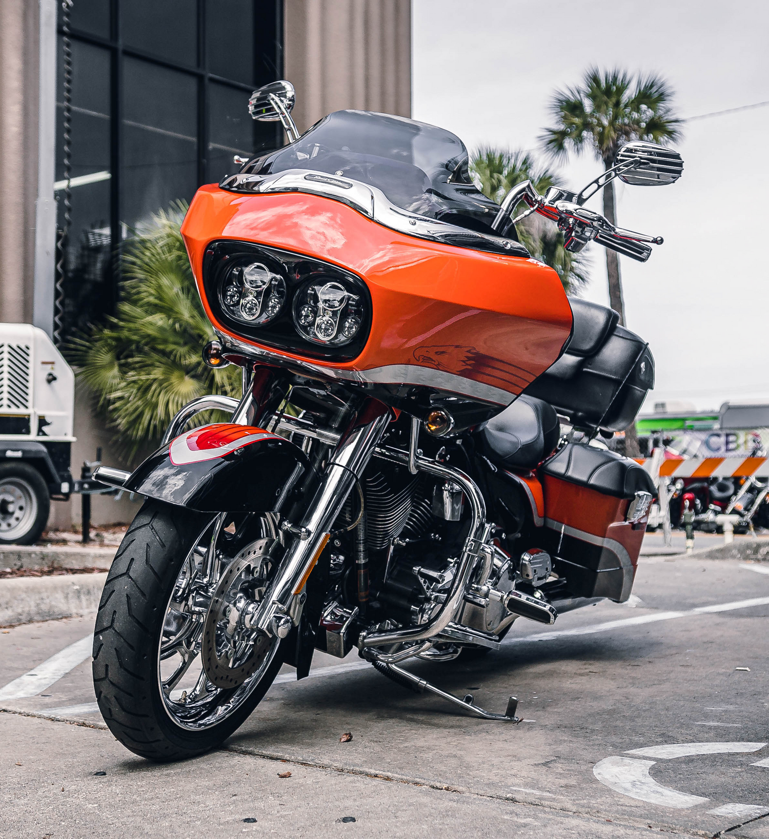Orange and black motorcycle parked on a city street with palm trees in the background.